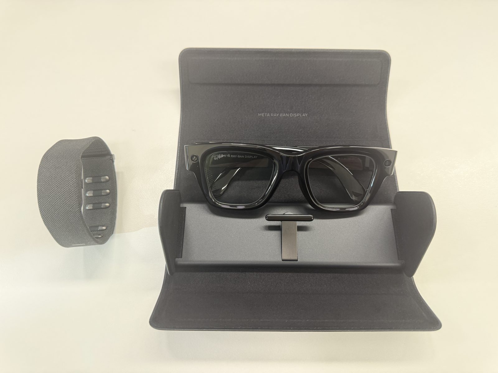 Meta Ray-Ban Display im geöffneten Ladeetui, darüber das graue Neural Band auf hellem Tisch